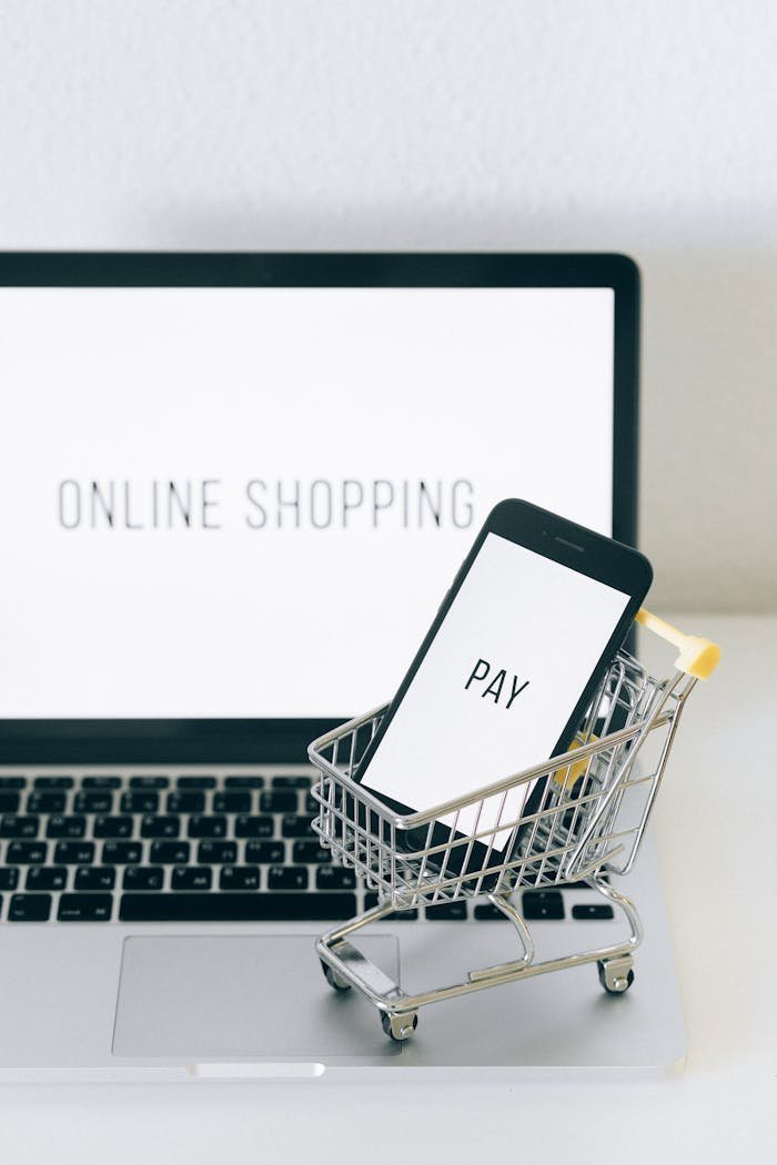 A smartphone in a miniature cart on a laptop symbolizes online shopping and digital payment.